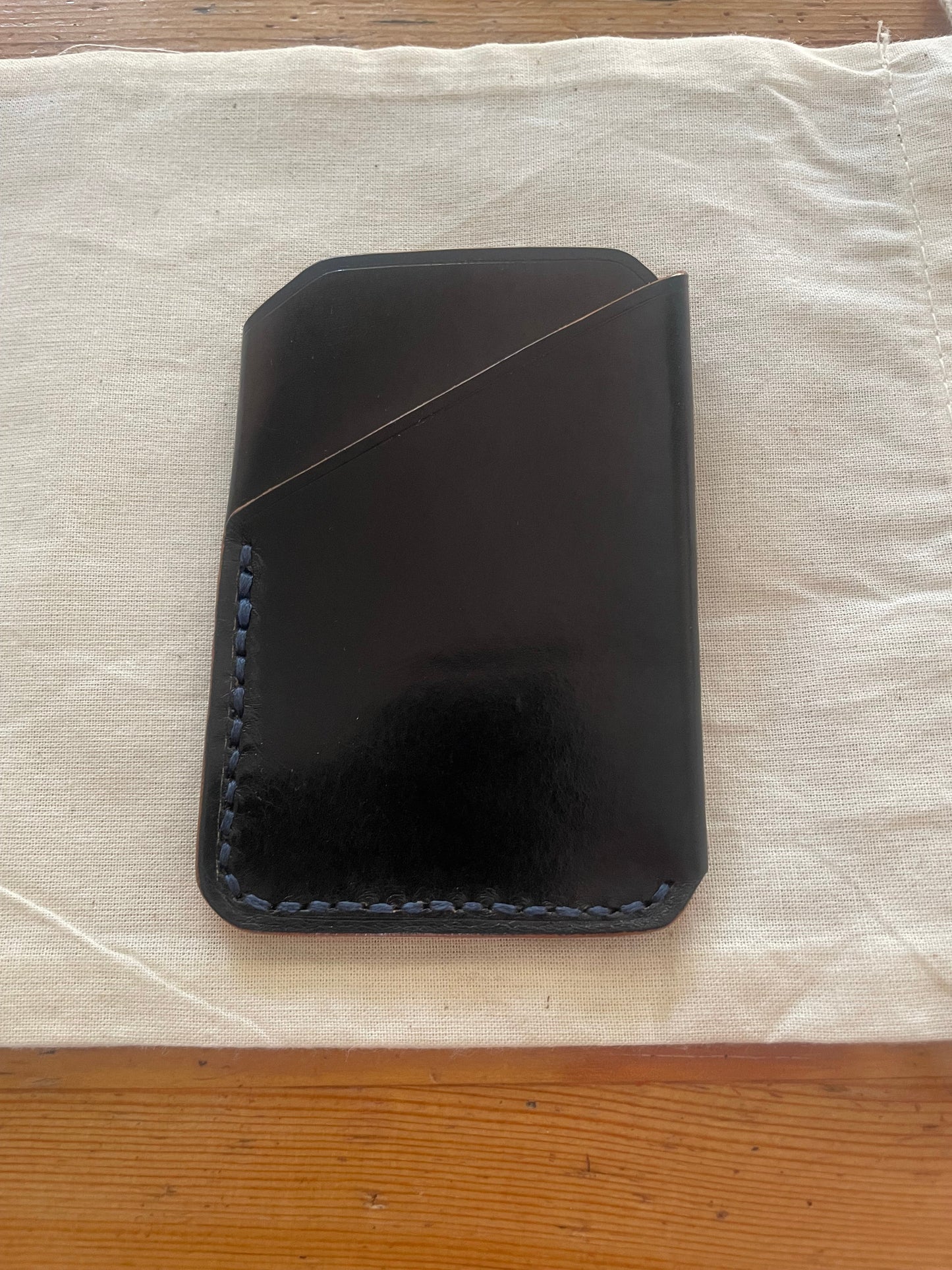 Handcrafted black leather card holder with dual pockets, minimalist design, and hand-stitched edges on a neutral fabric background.