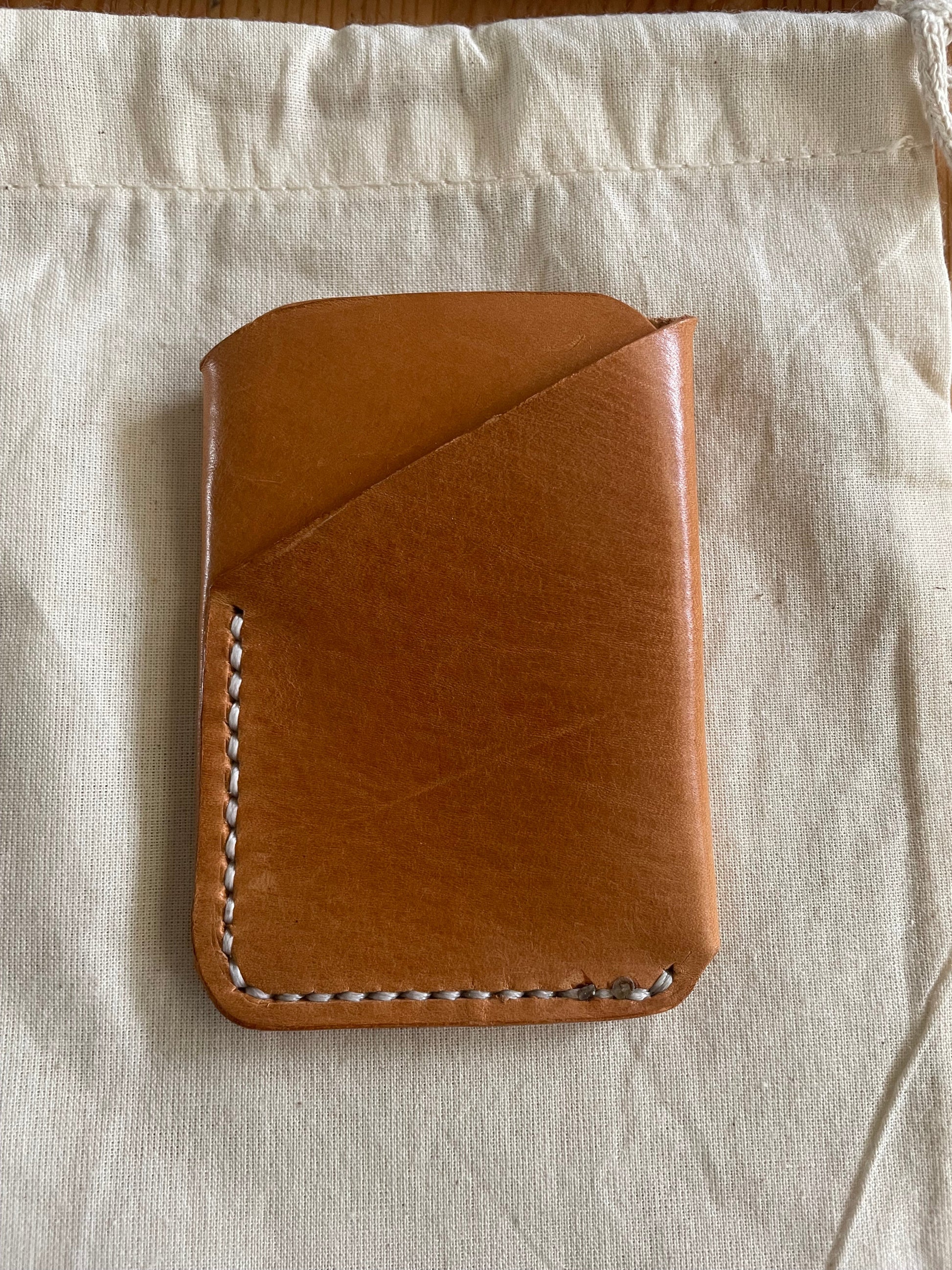 Handcrafted tan leather card holder with dual pockets, minimalist design, and hand-stitched edges on a neutral fabric background.