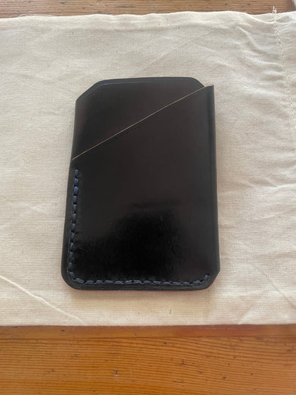 Handcrafted black leather card holder with dual pockets, minimalist design, and hand-stitched edges on a neutral fabric background.