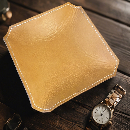 Tan leather tray on a wooden surface with a gold watch.